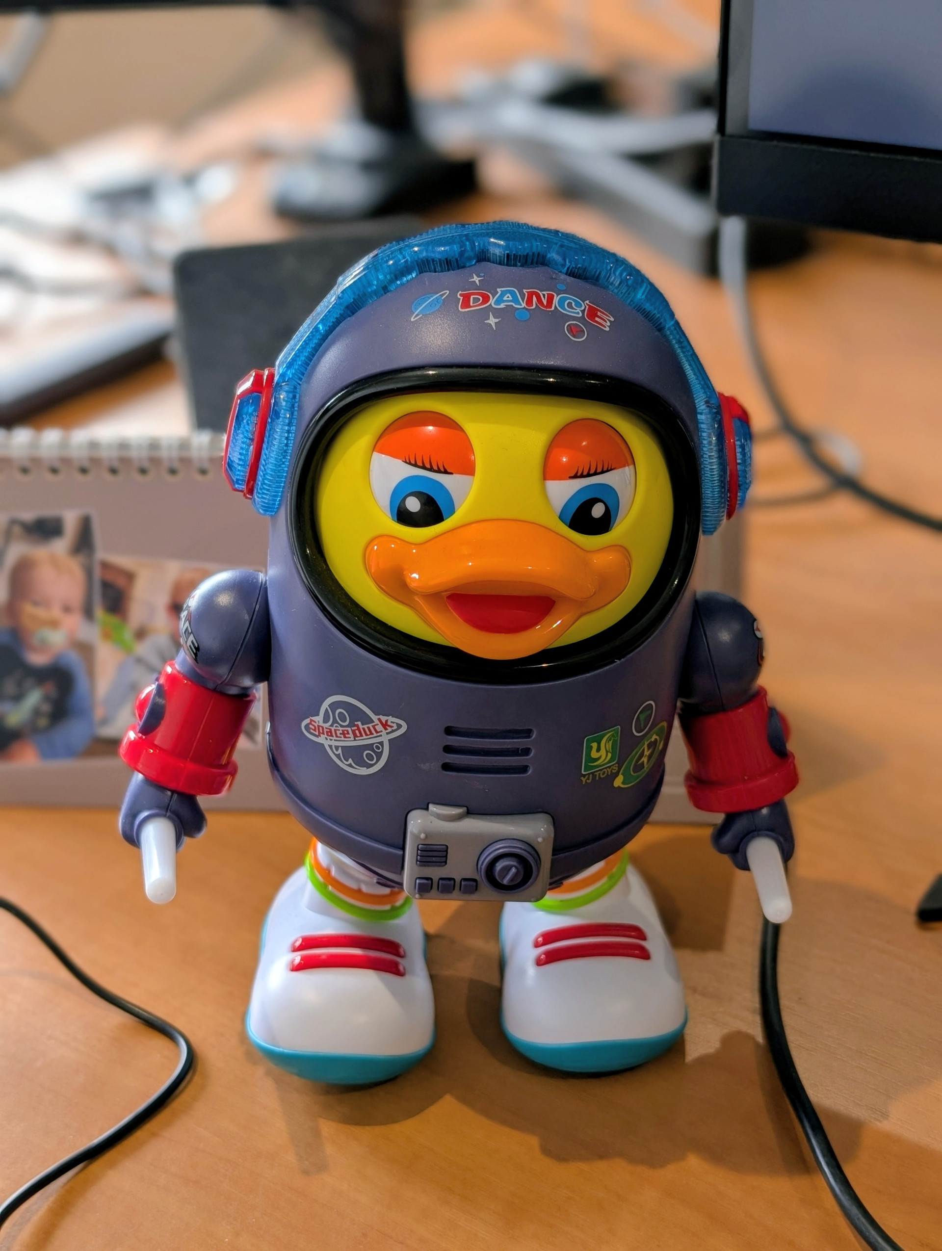 Blue and yellow space-themed toy robot featuring a large duck head, sitting on a desk.